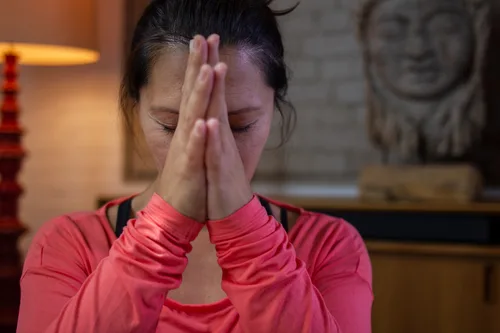 Porträt einer Frau mit vor dem Gesicht gefalteten Händen in rotem Oberteil, Titelbild der Seite ABJETZT/YOGA