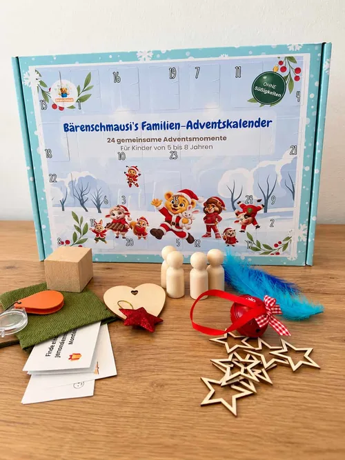 Bärenschmausis Familien-Adventskalender als hellblaue Schachtel mit 24 Türchen, davor Lupe, Holzfiguren, Glöckchen, Feder und Holzsterne