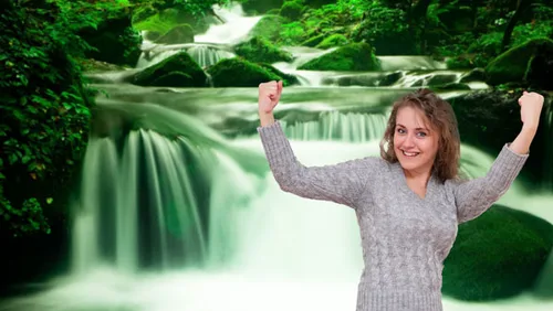 Kursbild zu Selbstheilungskräfte stärken: lächelnde Frau mit erhobenen Fäusten vor einem Wasserfall